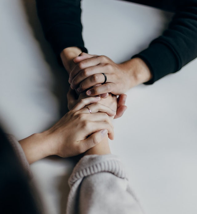 Two peoples' hands, clasped together and intertwined on a table