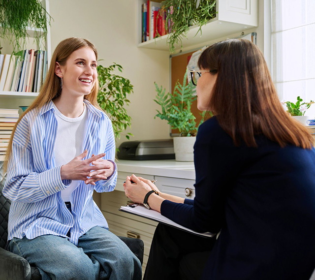 Young woman seated in a chair talking with another woman with a clipboard in her lap