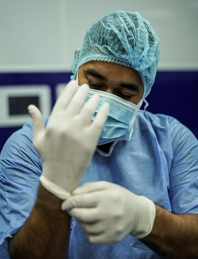 Person in blue medical scrubs putting on white gloves