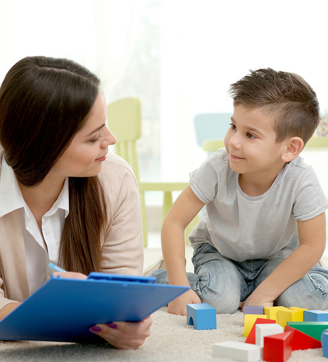 Young boy playing with blocks, smiling at a woman writing on a clipboard