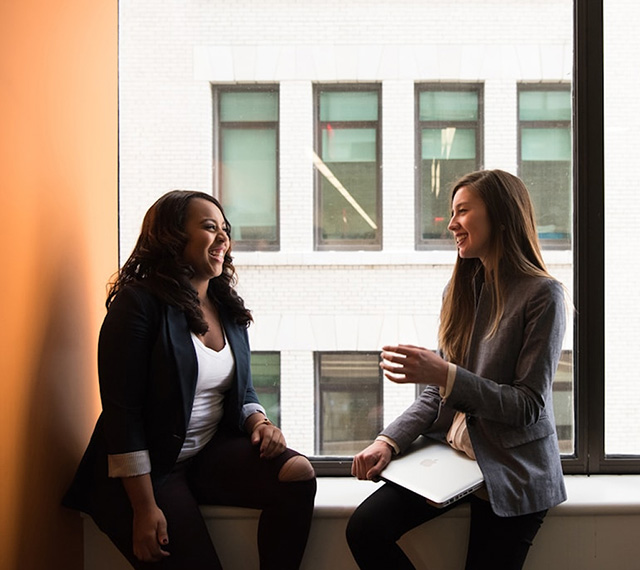 Two women seated on a window sill, chatting