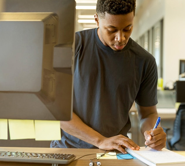 Man standing at a computer terminal, writing in a notebook