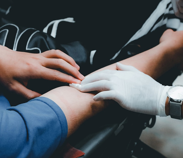 Hands pressing a piece of gauze in to a person's out-stretched arm