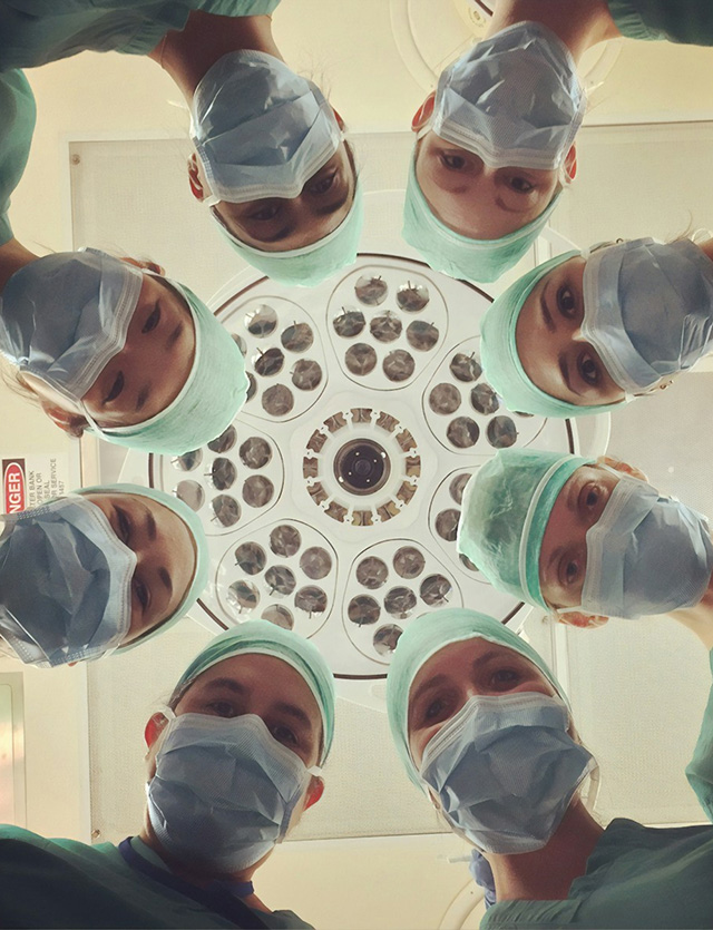 Masked medical professionals in an operating room glancing down at the operating table