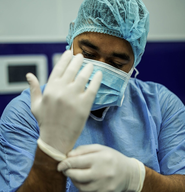Man in blue medical scrubs putting on white gloves