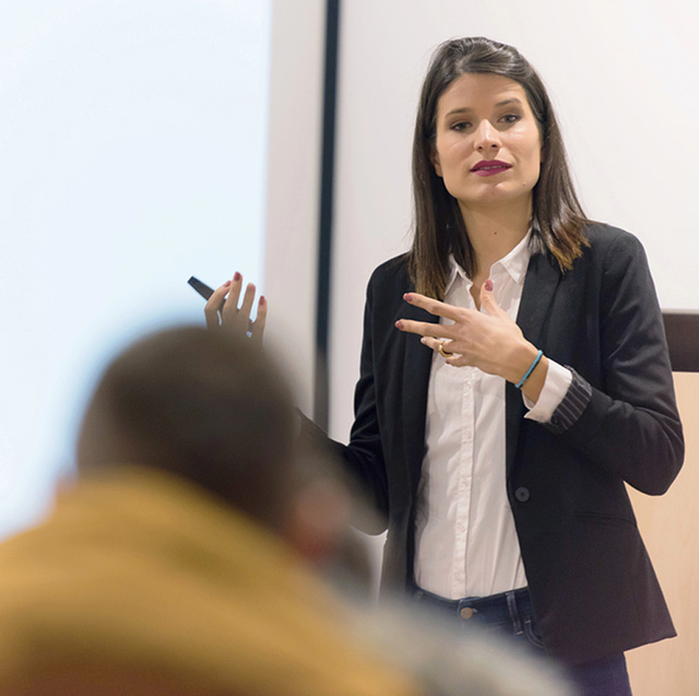 Woman standing on front of a classroom, gesturing with her hands