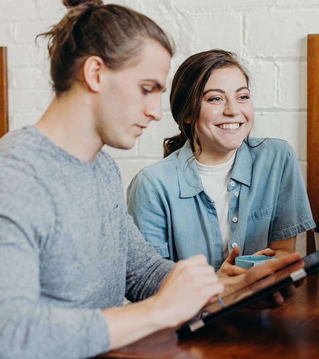 Young woman holding a mug and smiling while another person uses a tablet