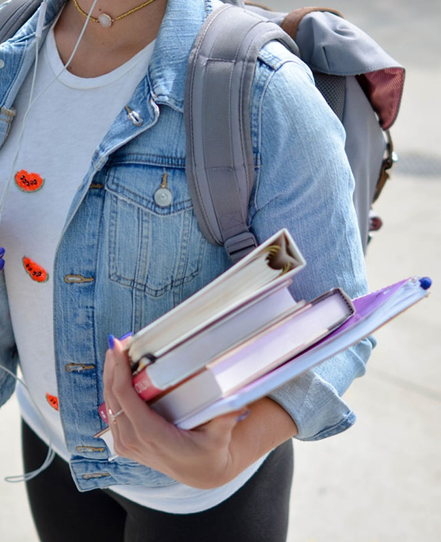 Close-up of a woman holding school books while wearing a backpack