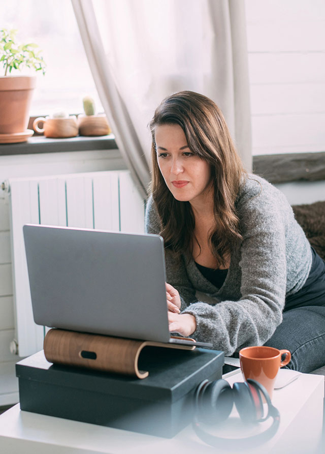 Seated woman in a gray sweater working on a laptop