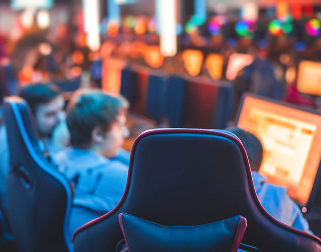 Gamers seated in gaming chairs at computer stations in a neon-lit esports venue.