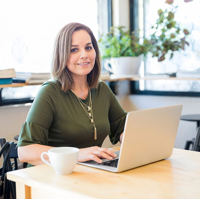 Woman seated at a table with her fingers on a laptop glancing at the camera