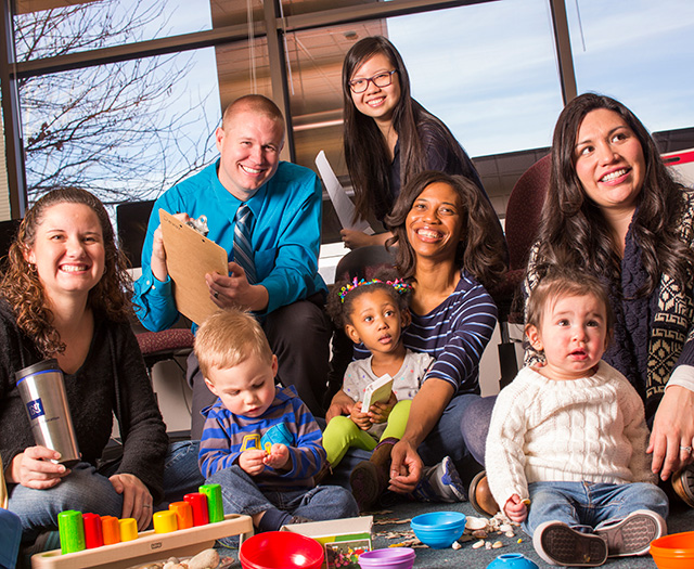 A group of seated adults and young children with various toys in the foreground