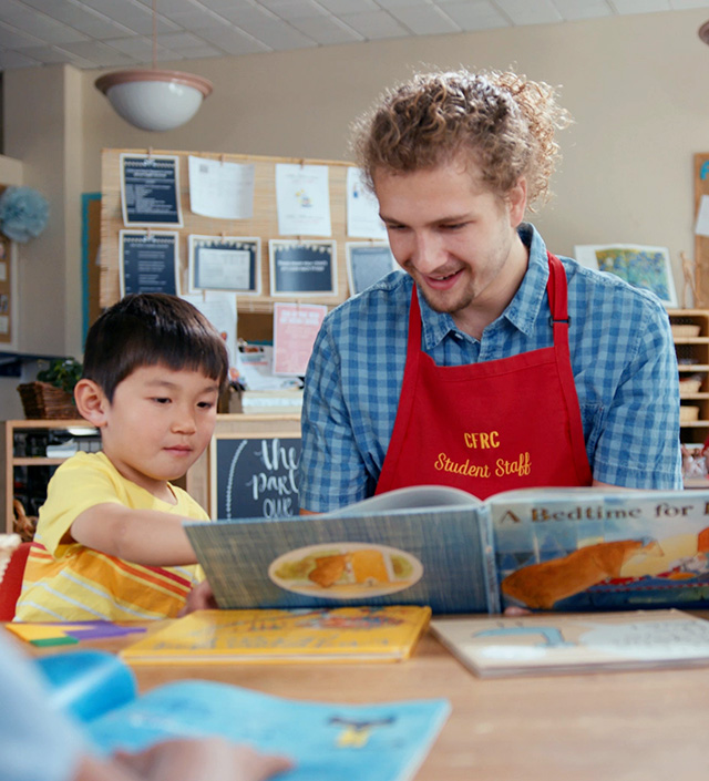 Young adult reading to a young child, who points at the open page