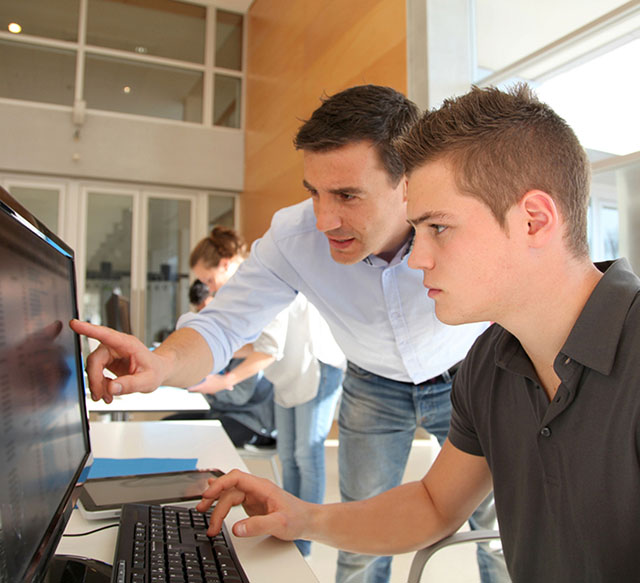 Man leaning over and point at a computer screen while another man types