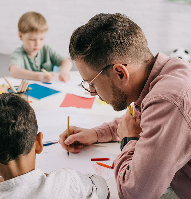 Man sitting at a table with young students, writing on a piece of paper