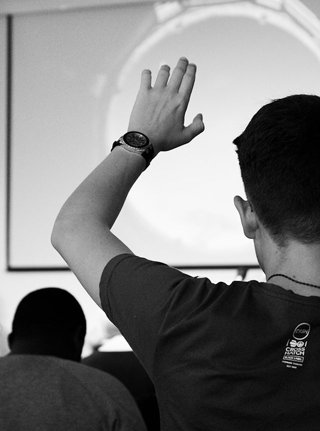 Student in a classroom raising his hand, seen from behind