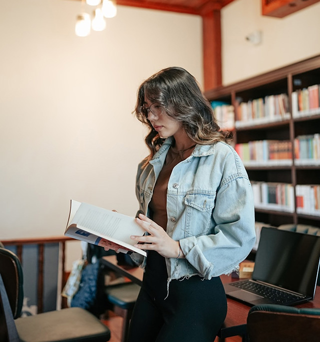 Student in a library partially seated on a table while reading a book