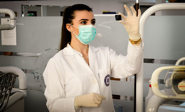 Woman in a white lab coat holding up an examining a small object in her left hand