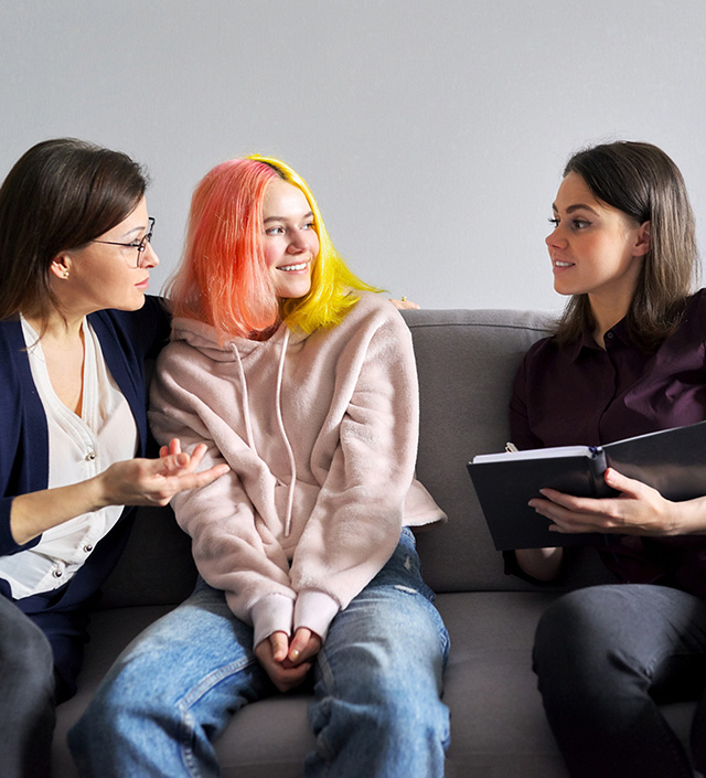 Three young women conversing on a couch while one takes notes