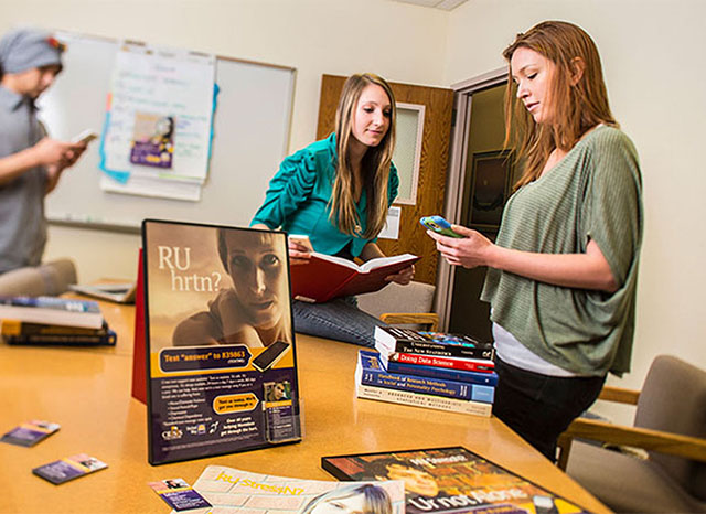 Woman in a conference room looking at her phone while another woman glances over