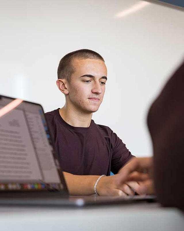 A young man with short hair looking down thoughtfully behind a laptop screen.