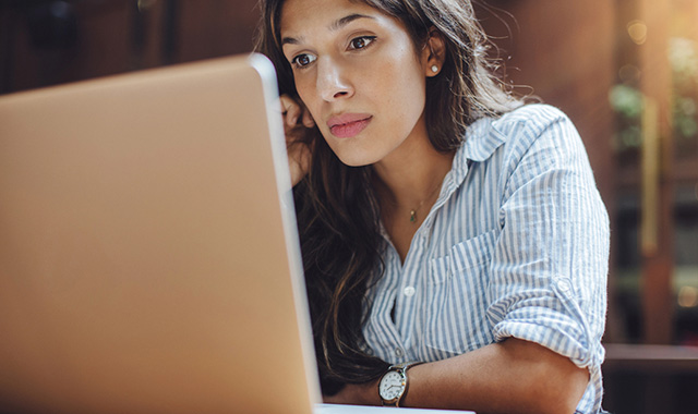 A woman looking thoughtfully at a laptop screen.