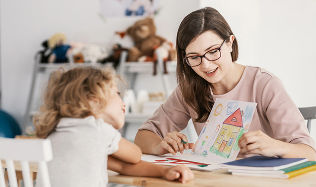A teacher showing a colorful drawing of a house to a young child.