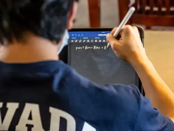 A student wearing a Nevada shirt works on a tablet at the University libraries.