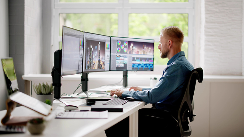 Person working at a desk with three computer monitors
