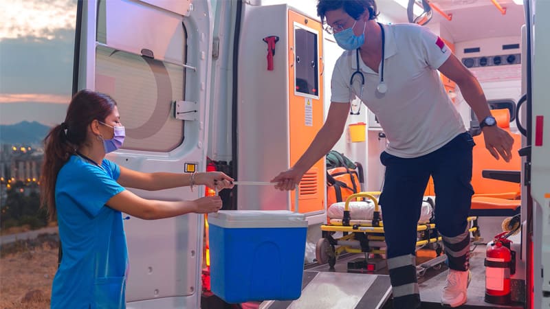 A transplantation coordinator passes a cooler from the back of an ambulance to an awaiting nurse.