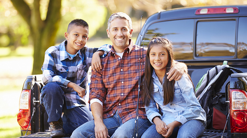 A man and two kids seated on the tailgate of a pickup truck, smiling at the camera