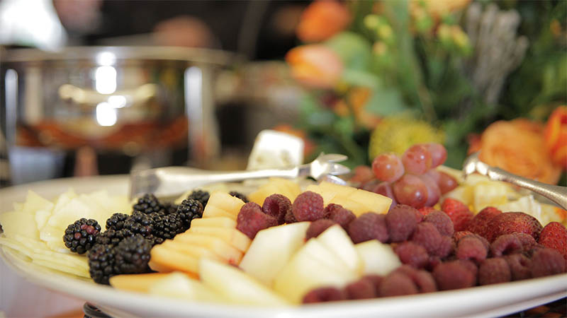 A plate of fruits, vegetables and cheeses, including blueberries, sliced applies and raspberries.