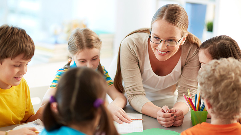 Woman interacting with elementary school kids seated at a table