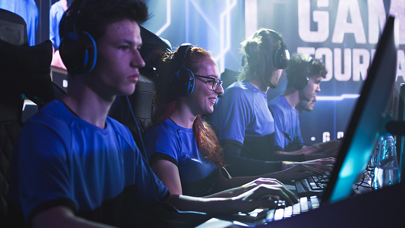 A team of esports players in matching blue jerseys and headsets gaming at a tournament.