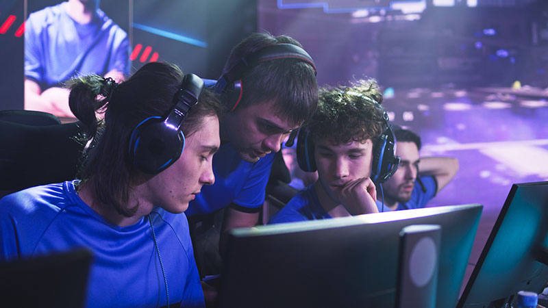 A team of esports players in matching blue jerseys and headsets gaming at a tournament.