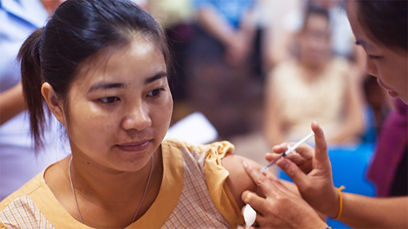Woman in a yellow shirt receiving an in injection in her left shoulder