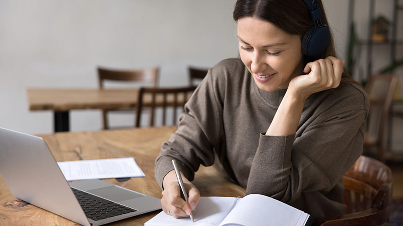 Woman seated at a table, writing in a notebook