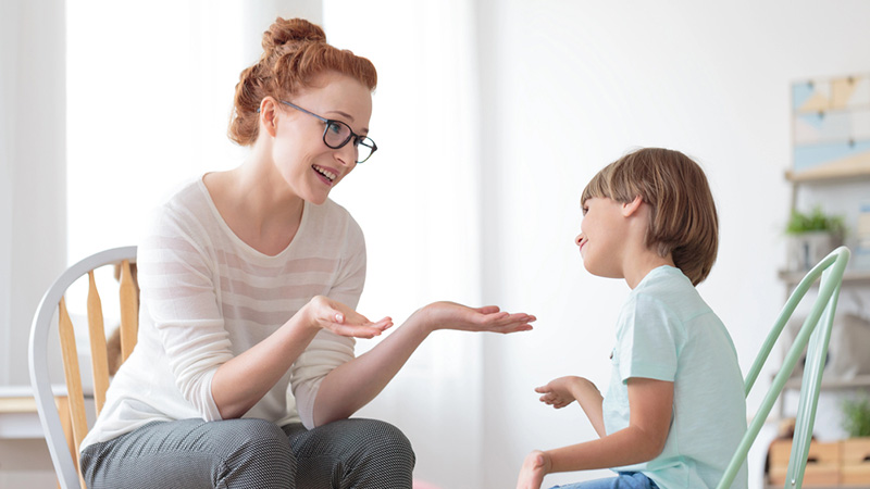 A therapist gesturing and communicating with a young boy.