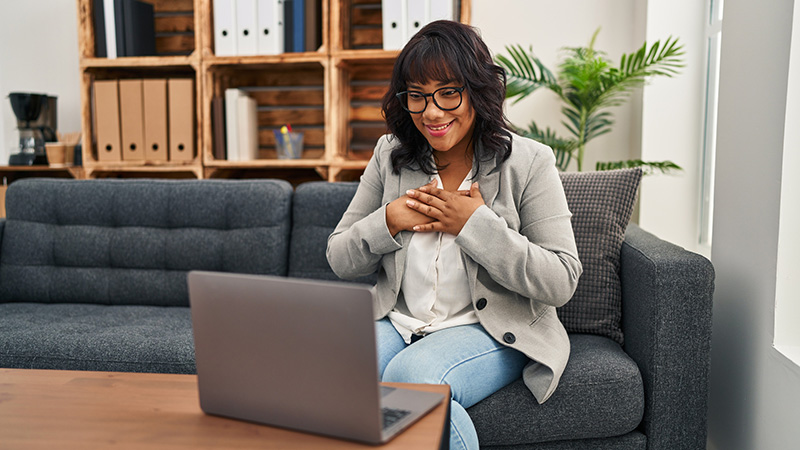 Woman seated on a couch, smiling while looking at a laptop screen