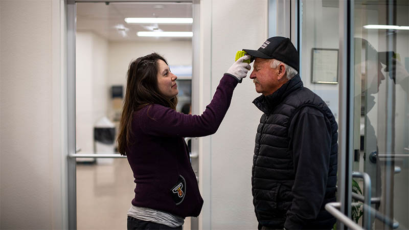 A nurse takes the temperature of a patient while standing in a hallway in a doctor's office.