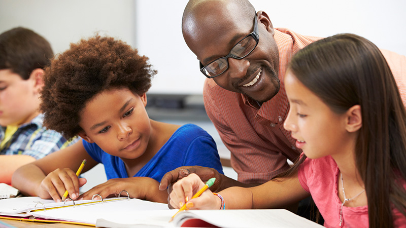 A teacher helping two young students with a writing exercise.