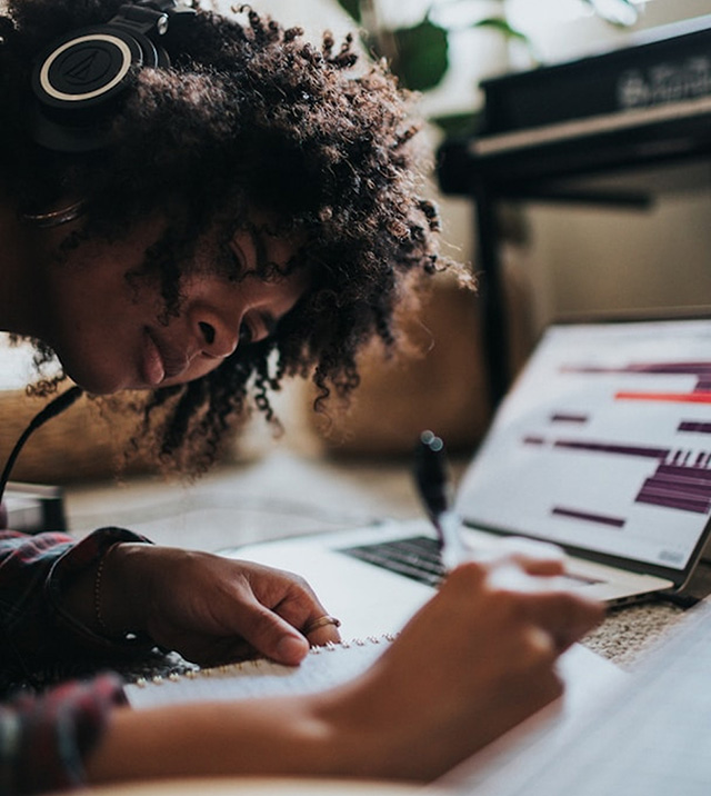 Woman writing in a notebook with an open laptop in the background