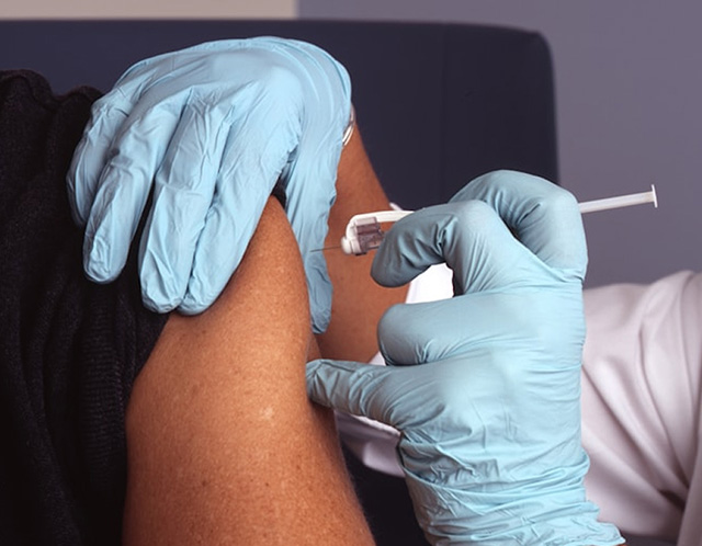 Blue-gloved hands giving in an injection in a person's shoulder