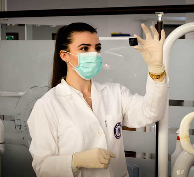 Woman in a white coat wearing rubber gloves holding up a small item to inspect it